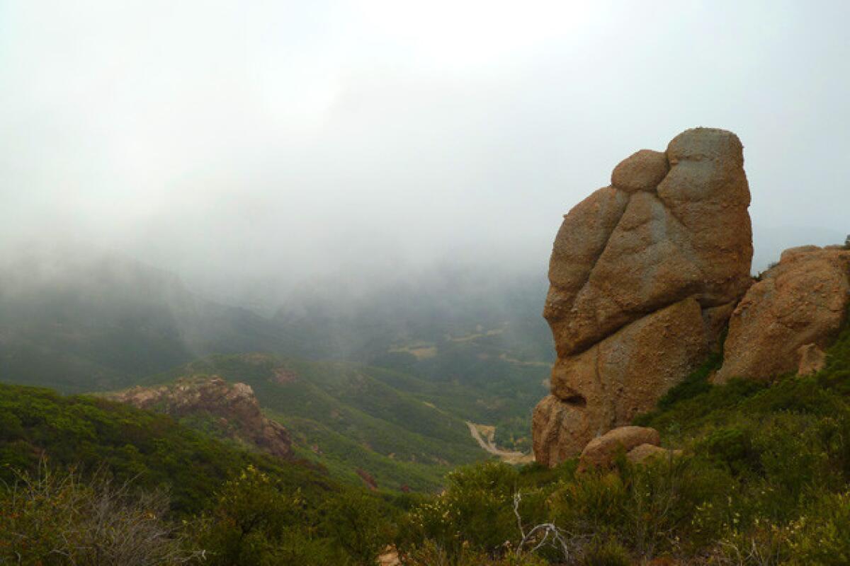 Brown boulders loom over a fog-enshrouded valley.