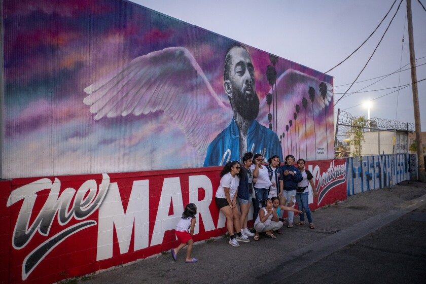 A group of people stand against a wall with a large mural of a man with angel's wings.