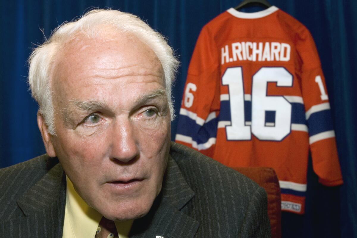 An elderly Henri Richard sitting in front of of his Montreal Canadiens jersey.