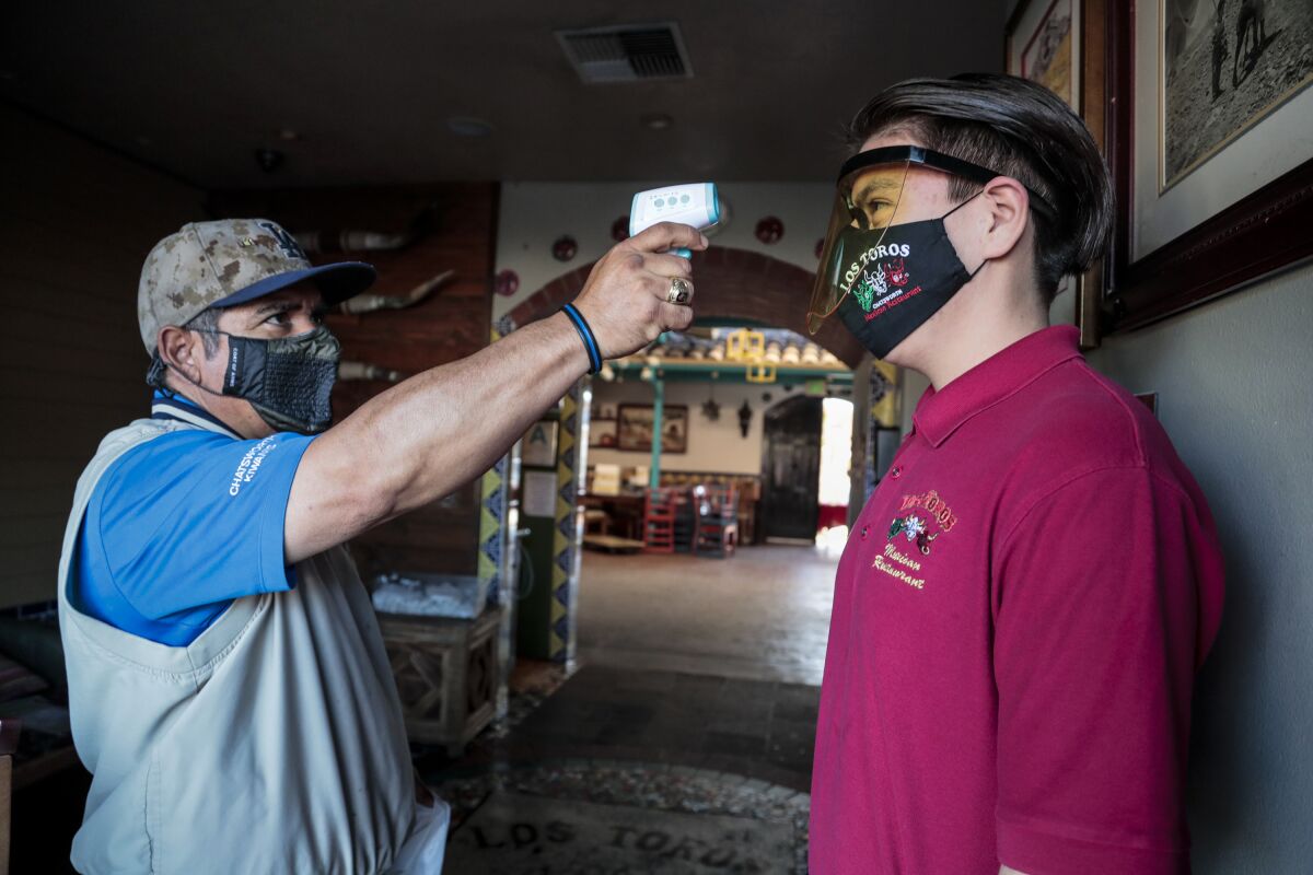 Nicolas Montaño uses a forehead scanner to check Diego Almendor's temperature
