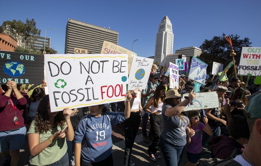 People hold up signs at a protest. One sign says: Do not be a fossil fool 