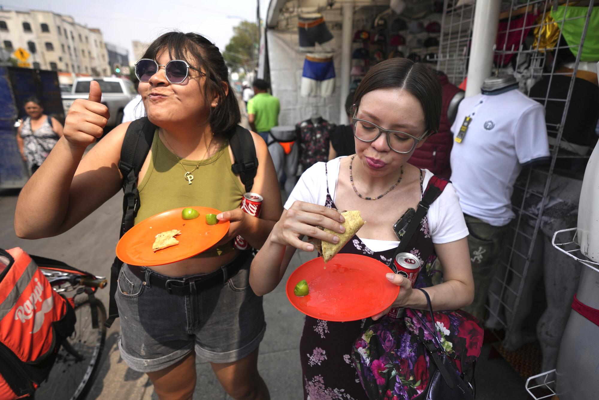 Two women, one smiling, enjoy their tacos. 