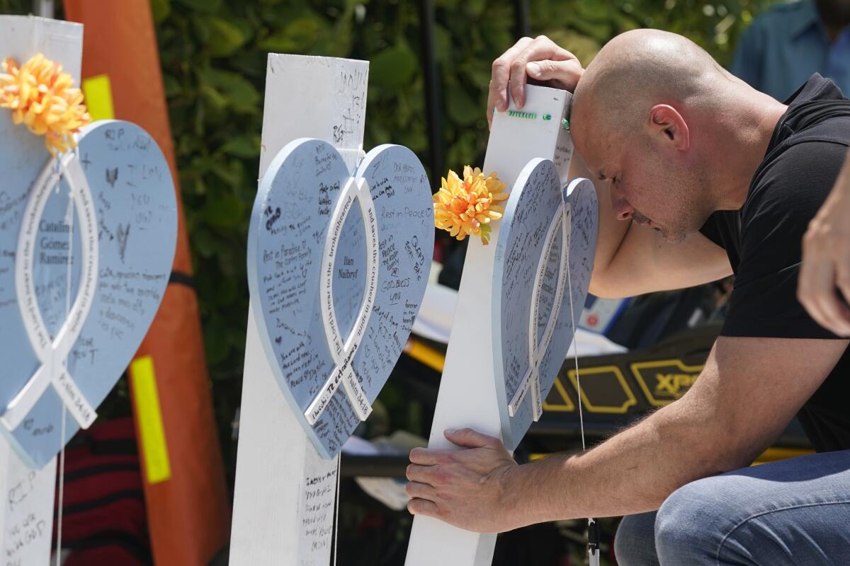 A man kneels down, placing his forehead against a memorial 