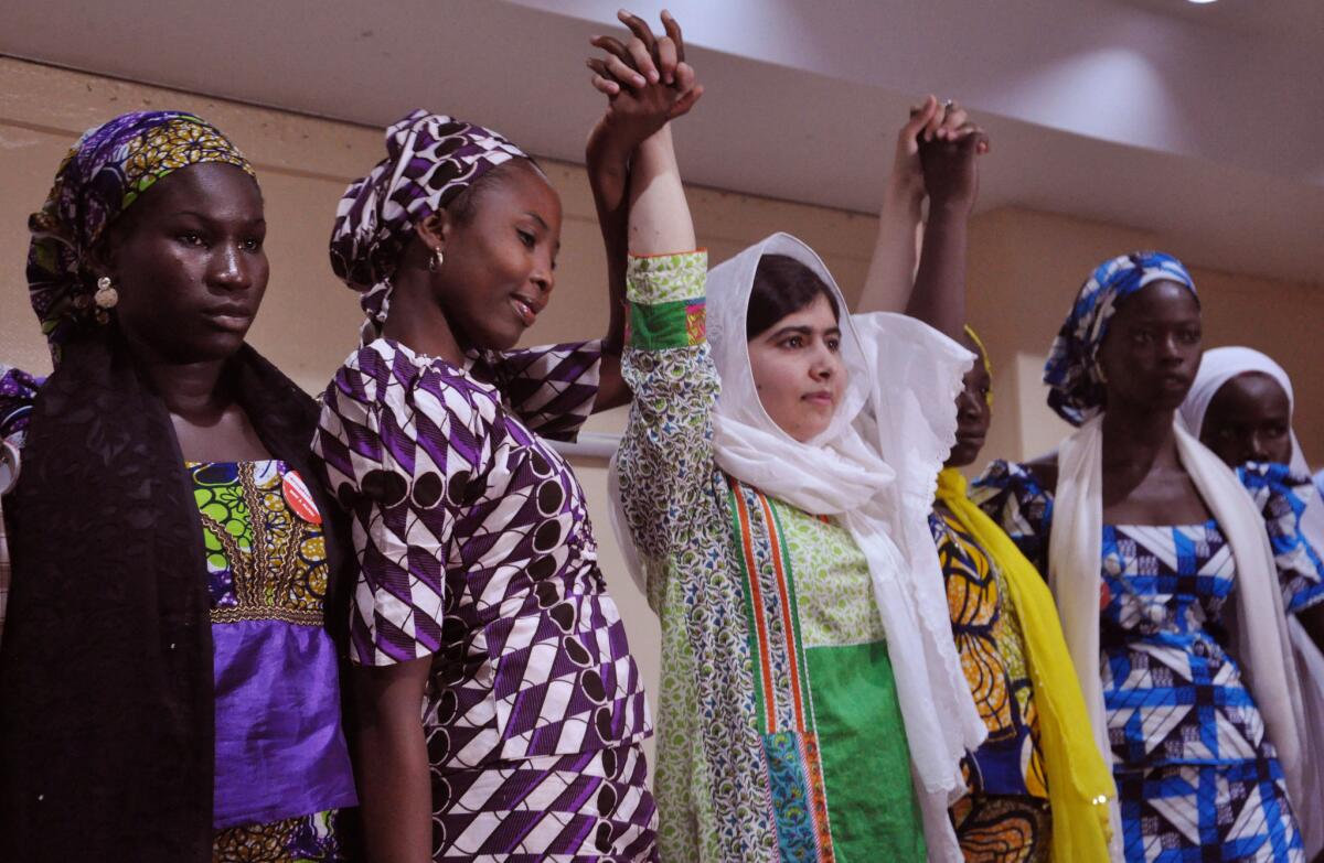 Pakistani activist Malala Yousafzai, center, raises her hands with some of the escaped kidnapped school girls of government secondary school Chibok, during a news conference, in Abuja, Nigeria on July 14, 2014. Yousafzai became the youngest Nobel Prize laureate in Oct. 2014, and two astronomers have named an asteroid they discovered after her.