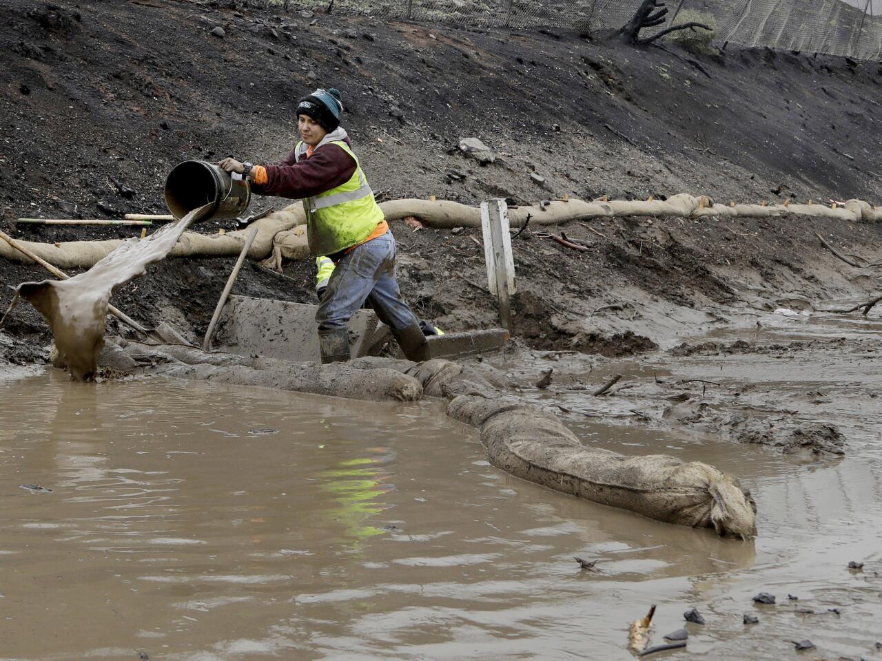A worker uses a bucket to clear out a drainage ditch along Pacific Coast Highway, north of El Matador Beach in Malibu.