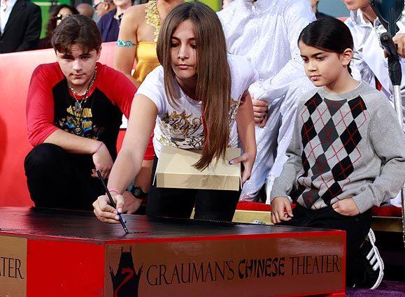 The three children of the late pop icon Michael Jackson immortalized their father in a hand and footprint casting ceremony at Grauman's Chinese Theatre in Hollywood. Paris Jackson writes Michael's name into the concrete as her brother Prince, left, and sister Blanket watch.