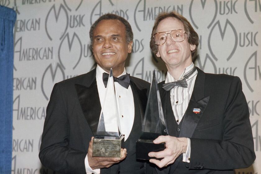FILE - Singer Harry Belafonte and Ken Kragen display their special awards presented to them in Los Angeles, on Jan. 28, 1986, during the 13th annual American Music Awards for their efforts in the "USA For Africa" project and the hit song "We Are The World." Kragen, a top entertainment producer, manager and philanthropist who turned to such clients as Lionel Richie and Kenny Rogers in helping to organize the 1985 all-star charity single “We Are the World,” has died at age 85. Kragen died Tuesday, Dec. 14, 2021, of natural causes at his home in Los Angeles, according to a statement released by his family. (AP Photo/Reed Saxon, File)