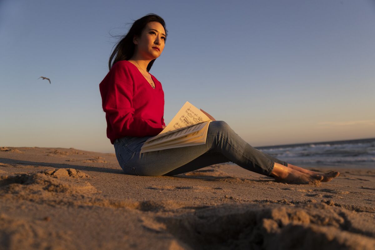 Pianist Sharon Su is shown holding sheet music on the beach at dusk 