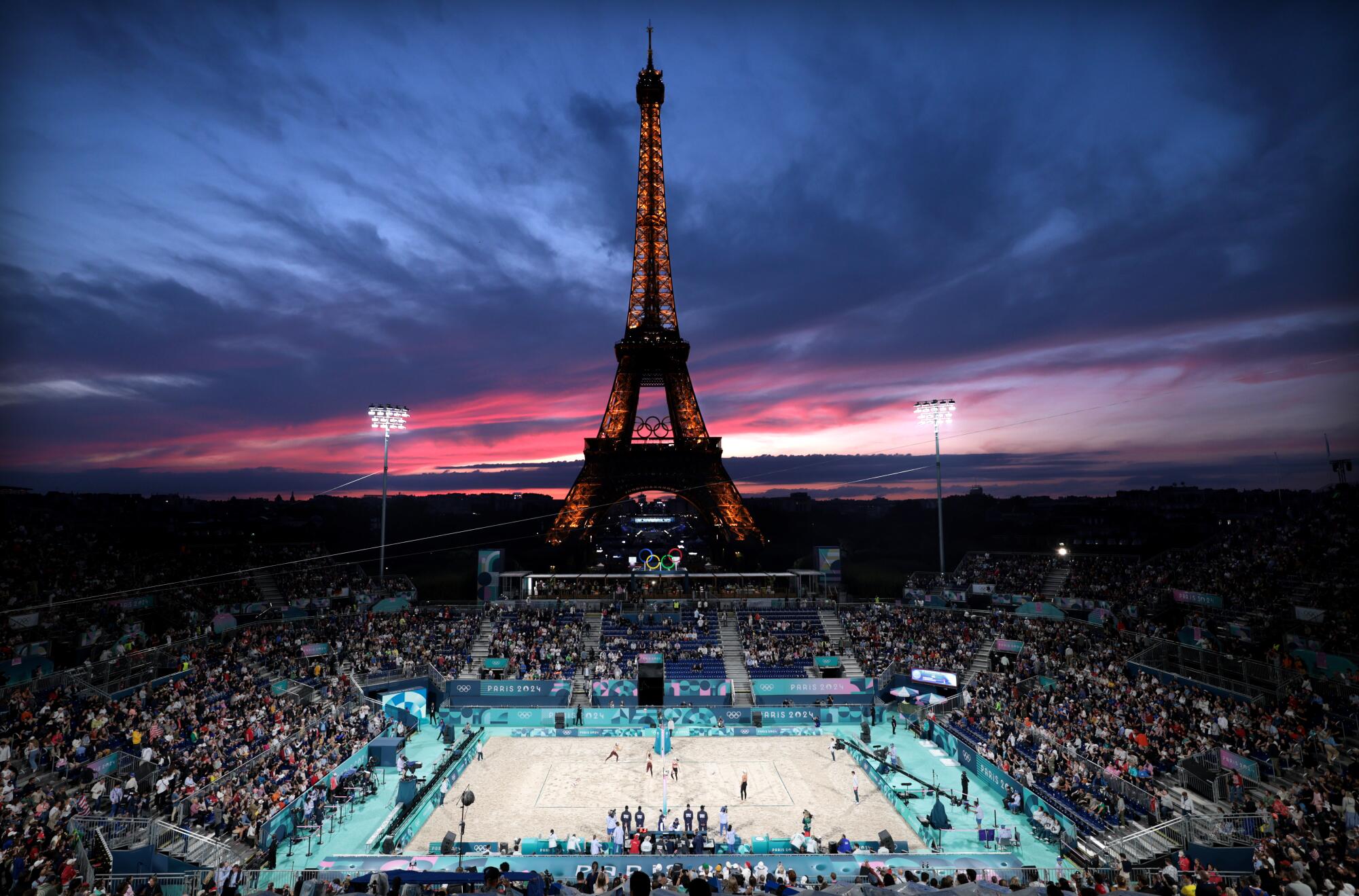 The sun sets over the Eiffel Tower as the U.S. and Canada women's beach volleyball teams warm up before a match.
