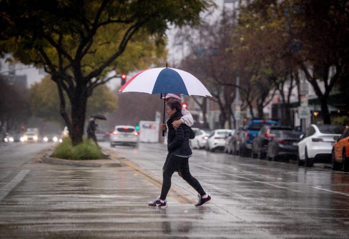 Pedestrians toting umbrellas walk across the street amidst heavy rain in Pasadena on Friday.