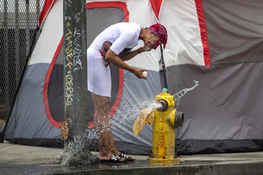 Los Angeles, CA - June 22: Yolanda Robins, 50, washes her face in water flowing from a fire hydrant in a skidrow on Wednesday, June 22, 2022, in Los Angeles, CA. In January, Yolanda Robins's dream was finally coming true. After three decades of living amid the squalor of Skid Row, occasionally punctuated by short stays in hotel rooms or shelters, she was approved to move into an apartment where she could begin to rebuild her life at 50 years old with help from a federal housing subsidy program. She is still living on the street. (Francine Orr / Los Angeles Times)