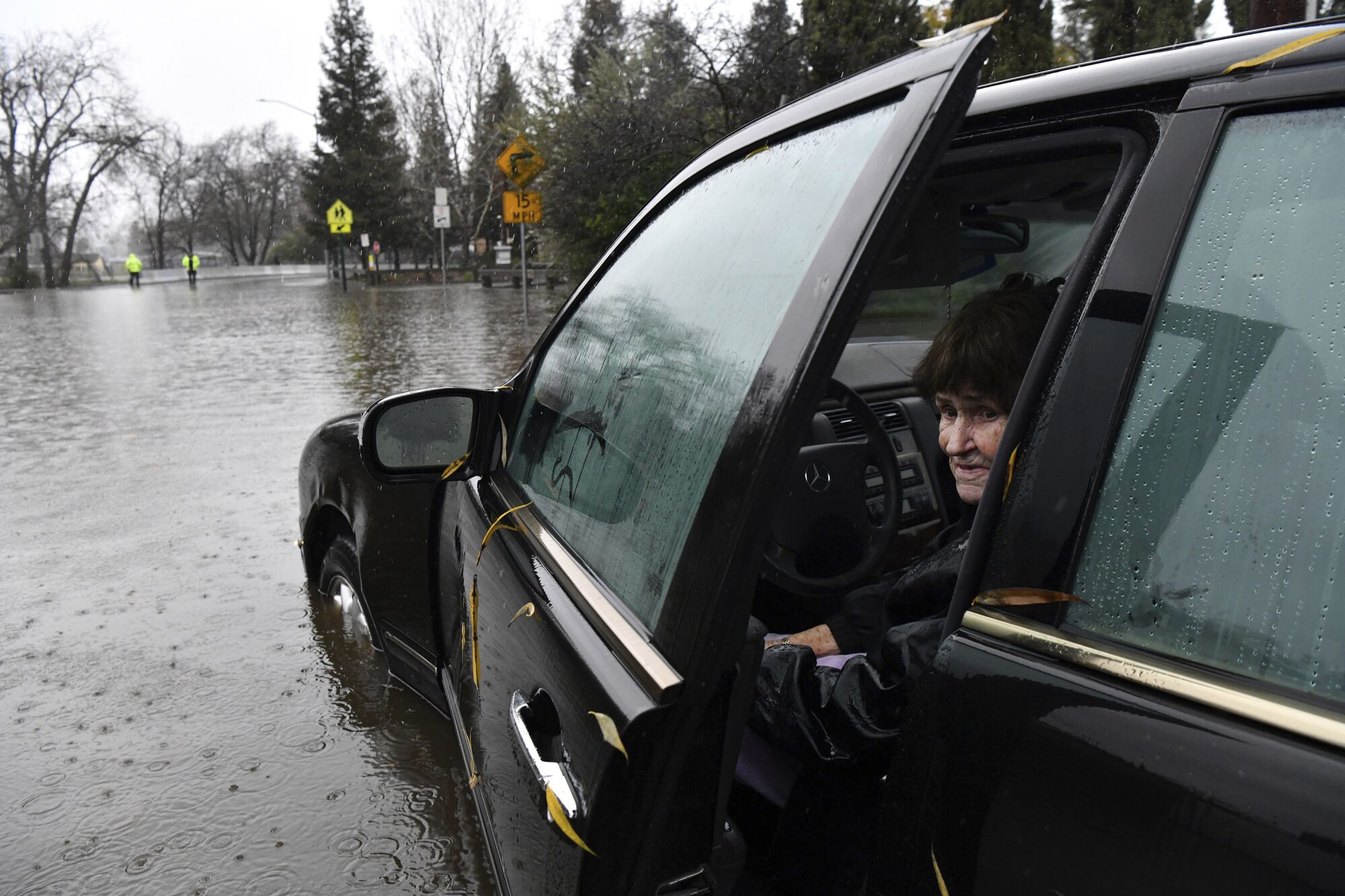 A woman peeks from an open door of her car, which is sitting in a flooded area.