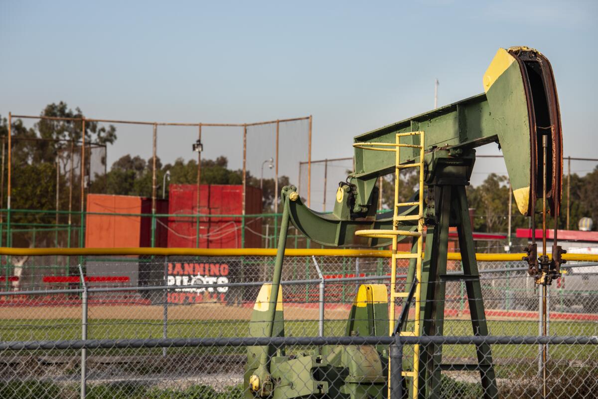 A green pumpjack, surrounded by wire fencing, sits near a baseball diamond 