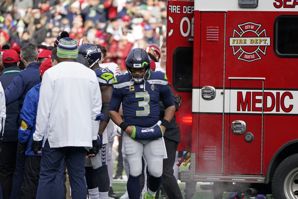 Seattle Seahawks quarterback Russell Wilson (3) stands near an ambulance before it took San Francisco 49ers running back Trenton Cannon off the field after an injury during the first half of an NFL football game at Lumen Field, Sunday, Dec. 5, 2021, in Seattle. (AP Photo/Elaine Thompson)