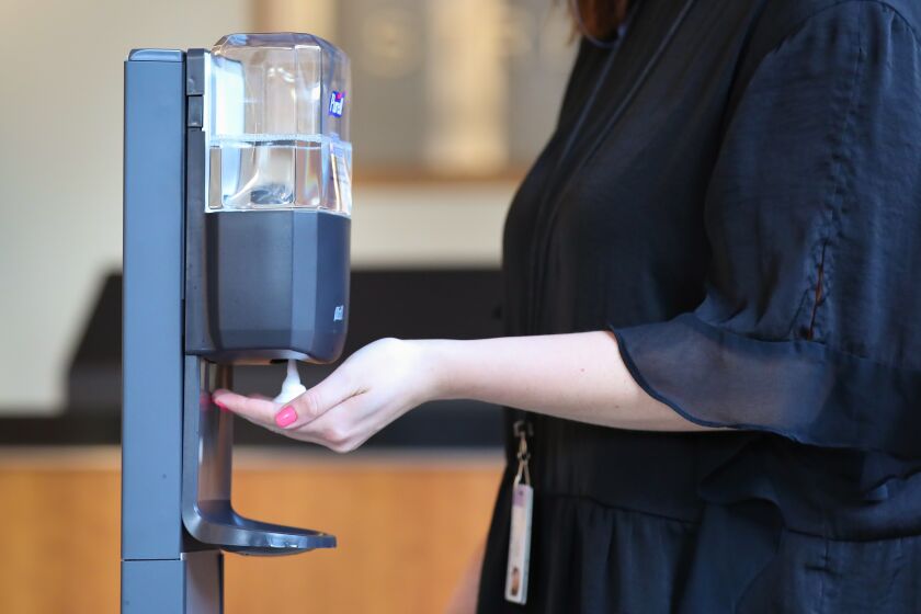 A person uses a hand sanitizer station in the lobby of a downtown San Diego office building, March 5, 2020.