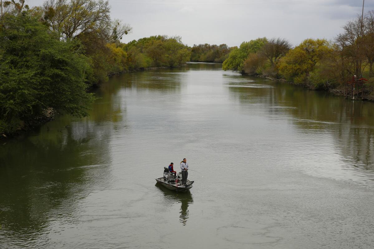 In a calm body of water surrounded by trees, people fish from a small boat.