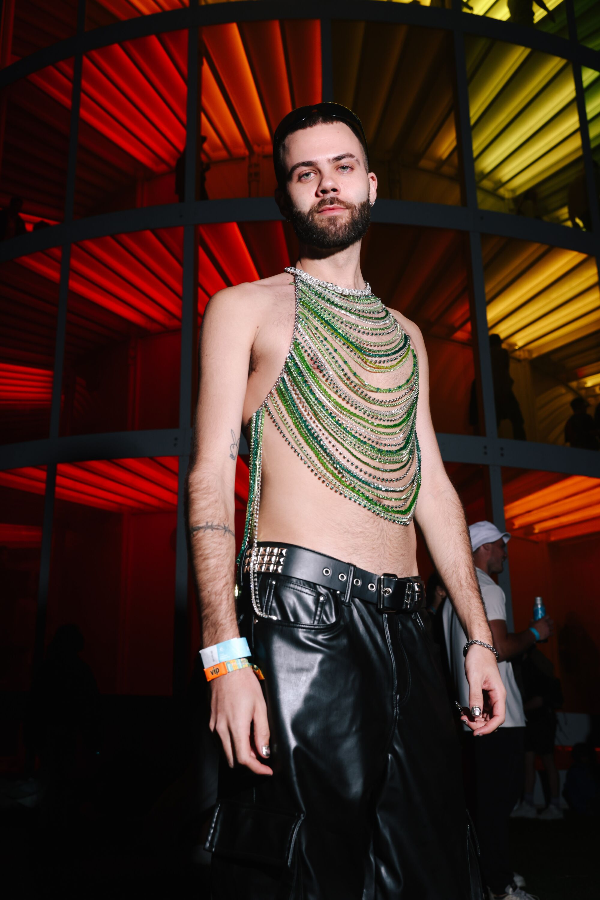 A man wearing chains poses in front of an art piece