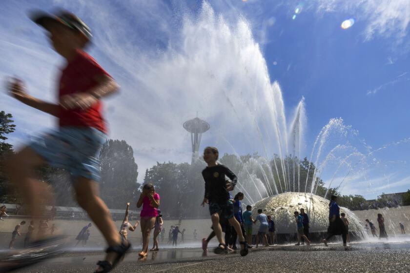 The International Fountain at Seattle Center is packed with children as they run from the water that is showering on them Wednesday, July 27, 2022 in Seattle. (Ellen M. Banner/The Seattle Times via AP)