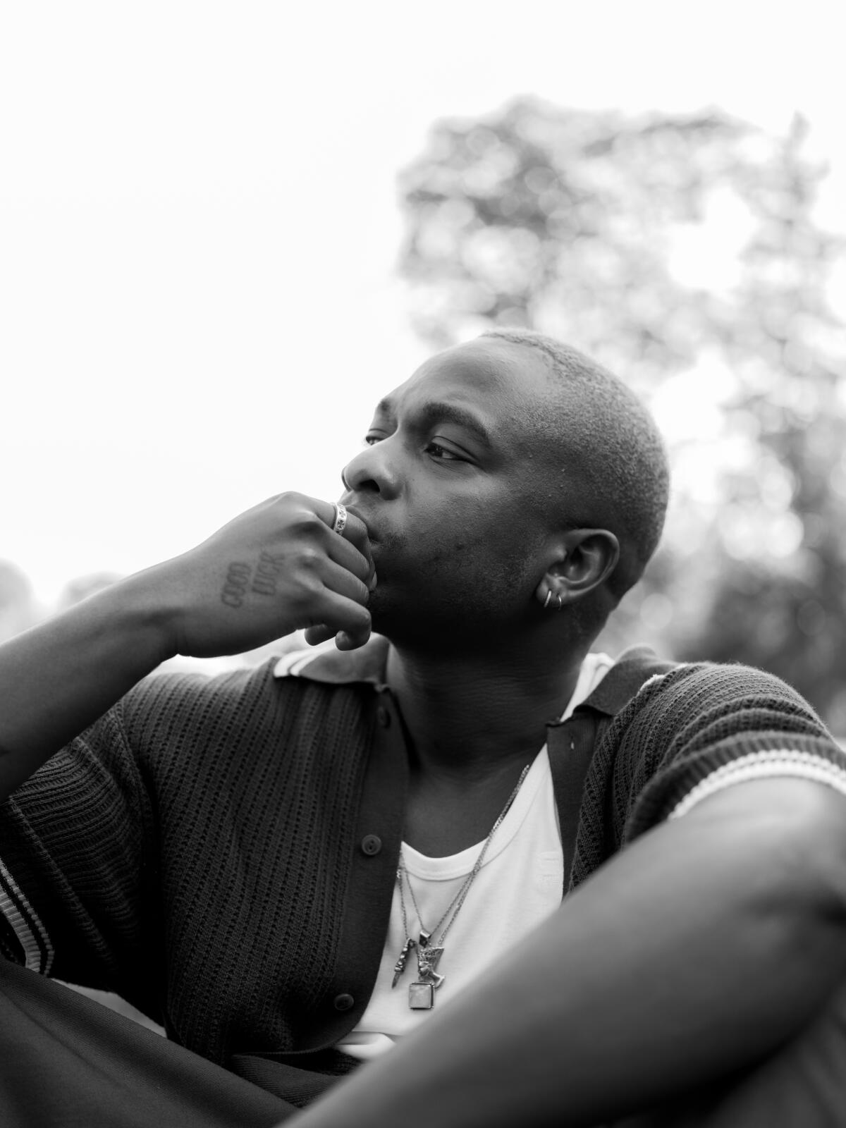 A man sits outdoors, his hand to his chin.