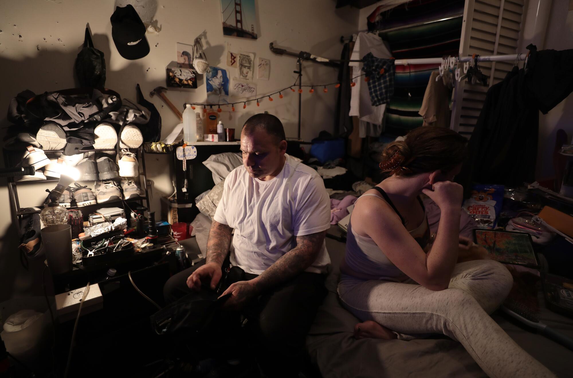 Two people sit in a cluttered room