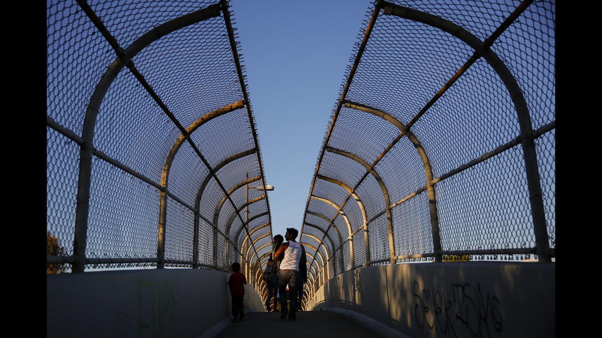 Jose Franco, with Jose Jr., 2, in his arms and Joshua, 5, at his side, use a pedestrian walkway to cross over the 60 Freeway from the southern to the northern part of Belvedere Park.