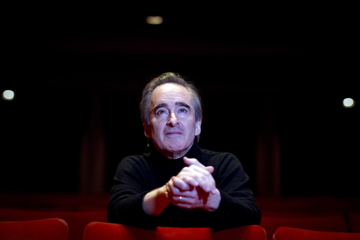 James Conlon, wearing a black shirt, is seen sitting amid rows of red theater seats.