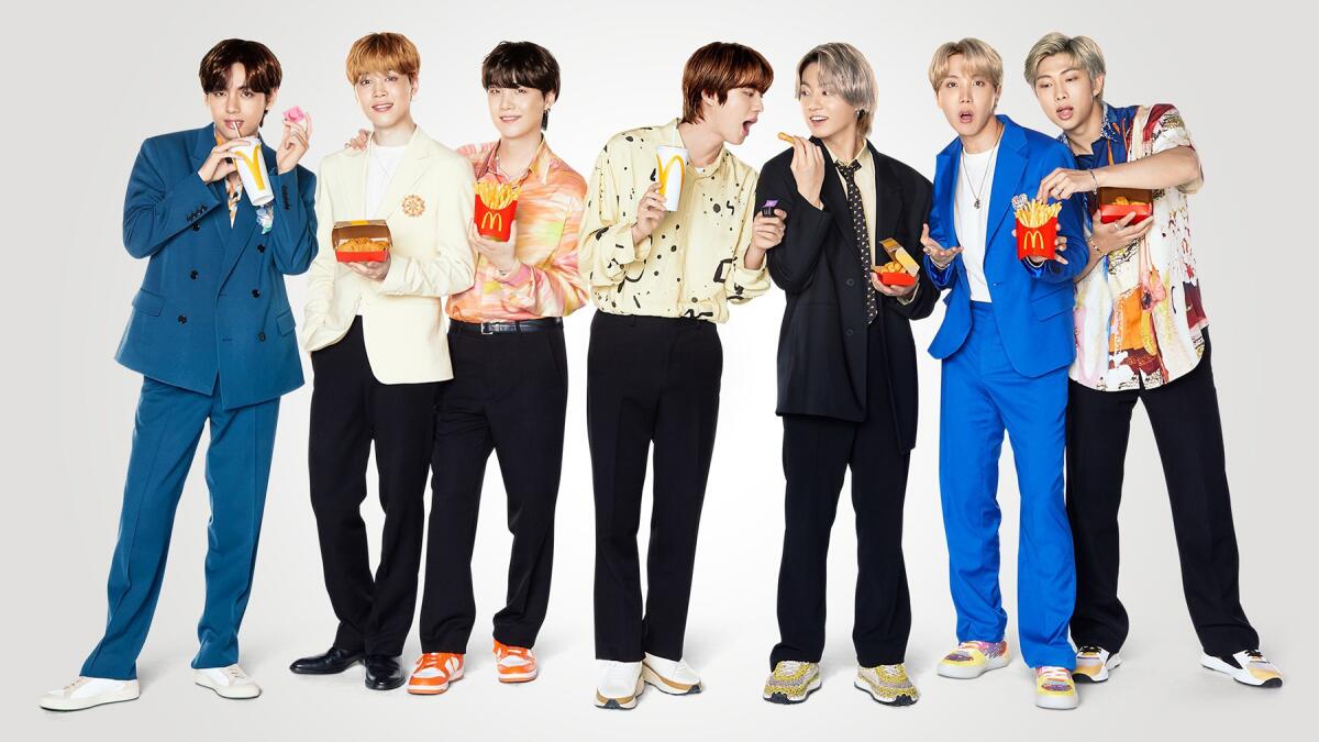 The seven members of BTS stand in a line, holding McDonald's food and drink