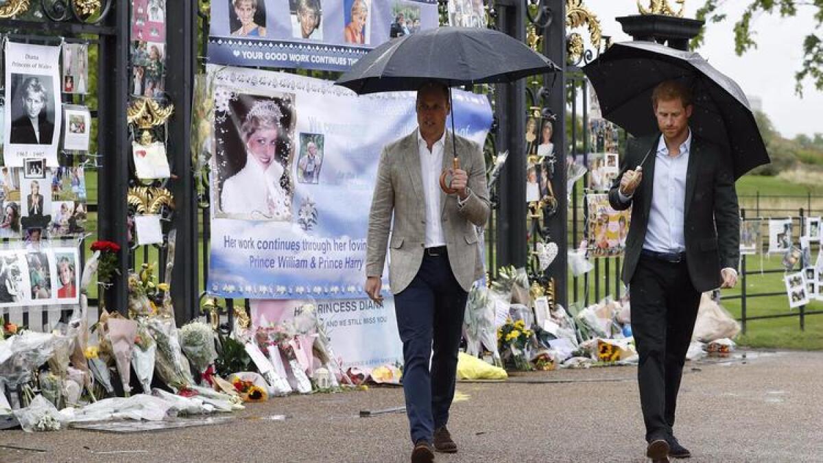 Prince William, left, and Prince Harry look at tributes left by members of the public outside Kensington Palace in London to mark the 20th anniversary of the death of their mother.