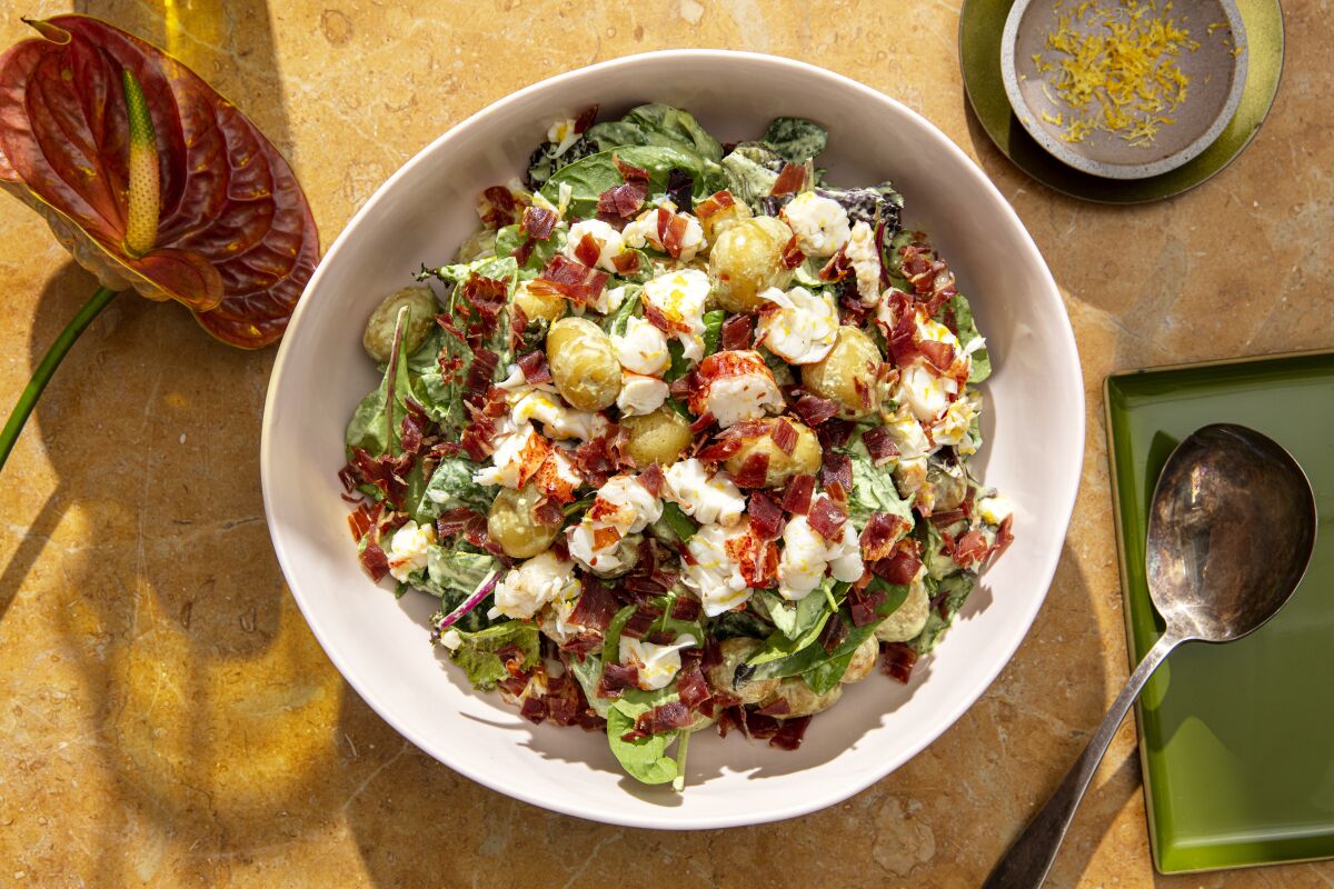 A white bowl of potato salad includes leafy greens.