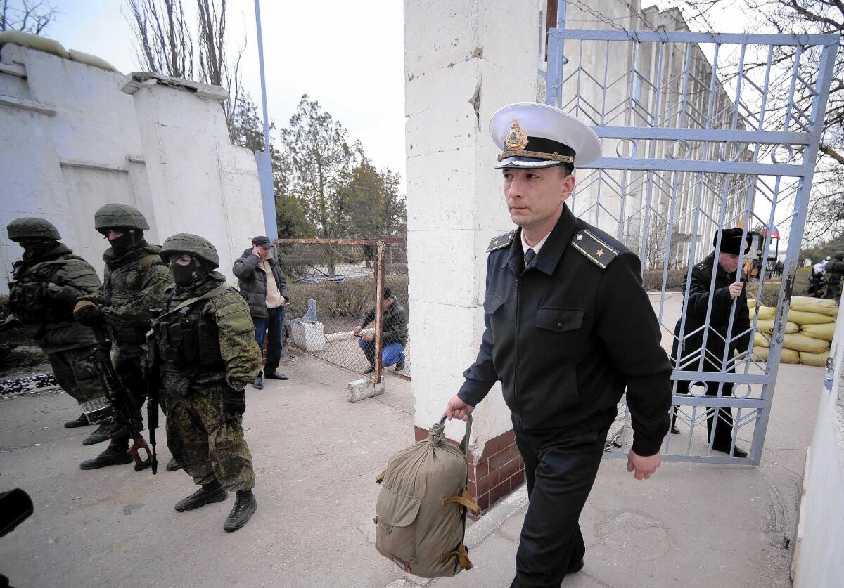 A Ukrainian officer leaves as Russian soldiers stand guard after taking control of a Ukrainian naval base in Crimea.