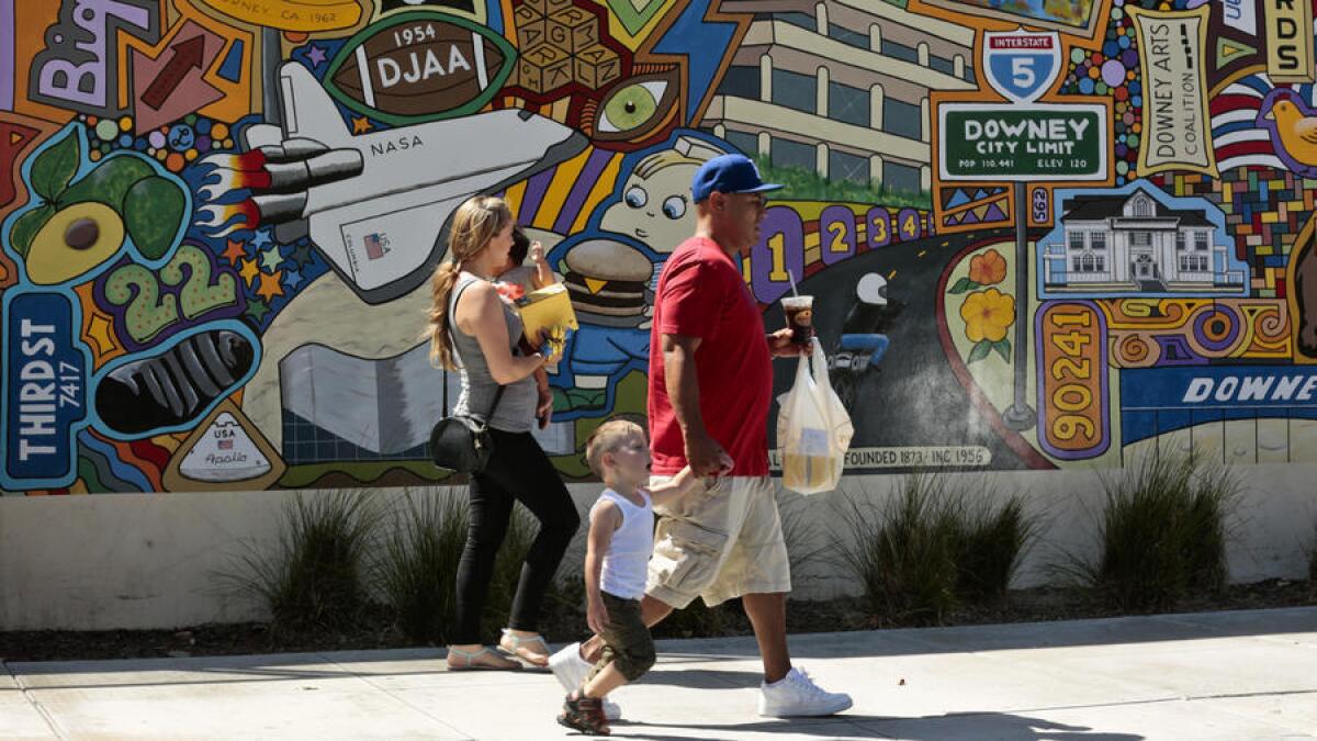 Una familia camina frente a un mural en Downey Avenue mientras llevan su comida del famoso Porto’s Bakery and Cafe. El mural representa la diversidad de este suburbio de clase media en Downey, antigua casa del transbordador espacial.