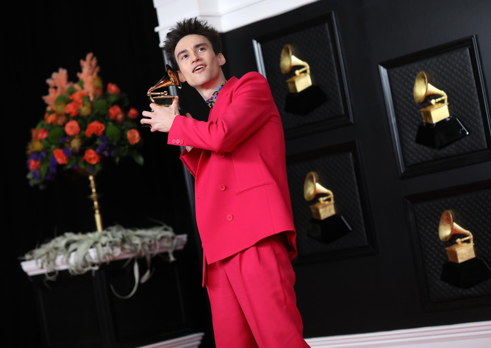Jacob Collier, in a red suit, holds his Grammy award.