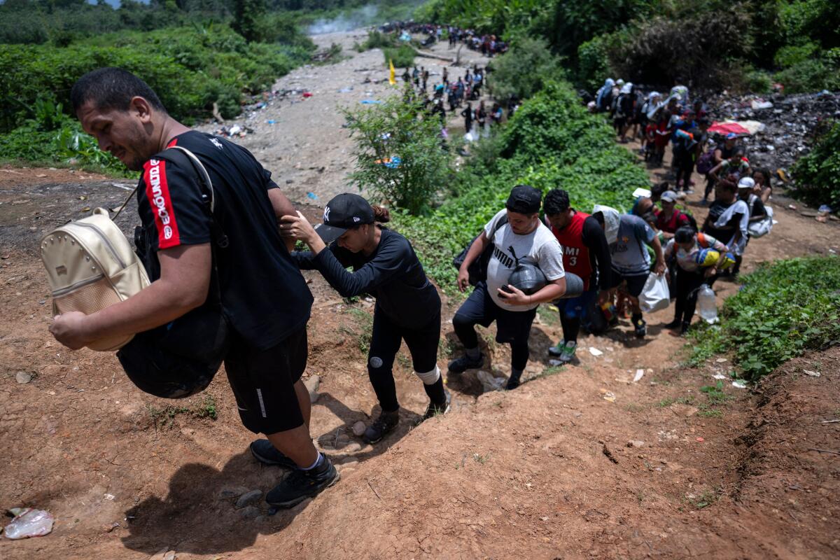 A long line of migrants walking single-file on a dirt trail up a hillside