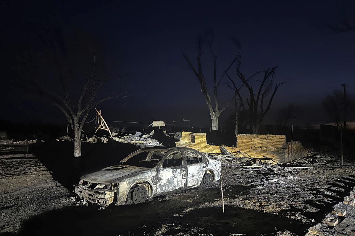A charred vehicle sits near the ruins of a home.