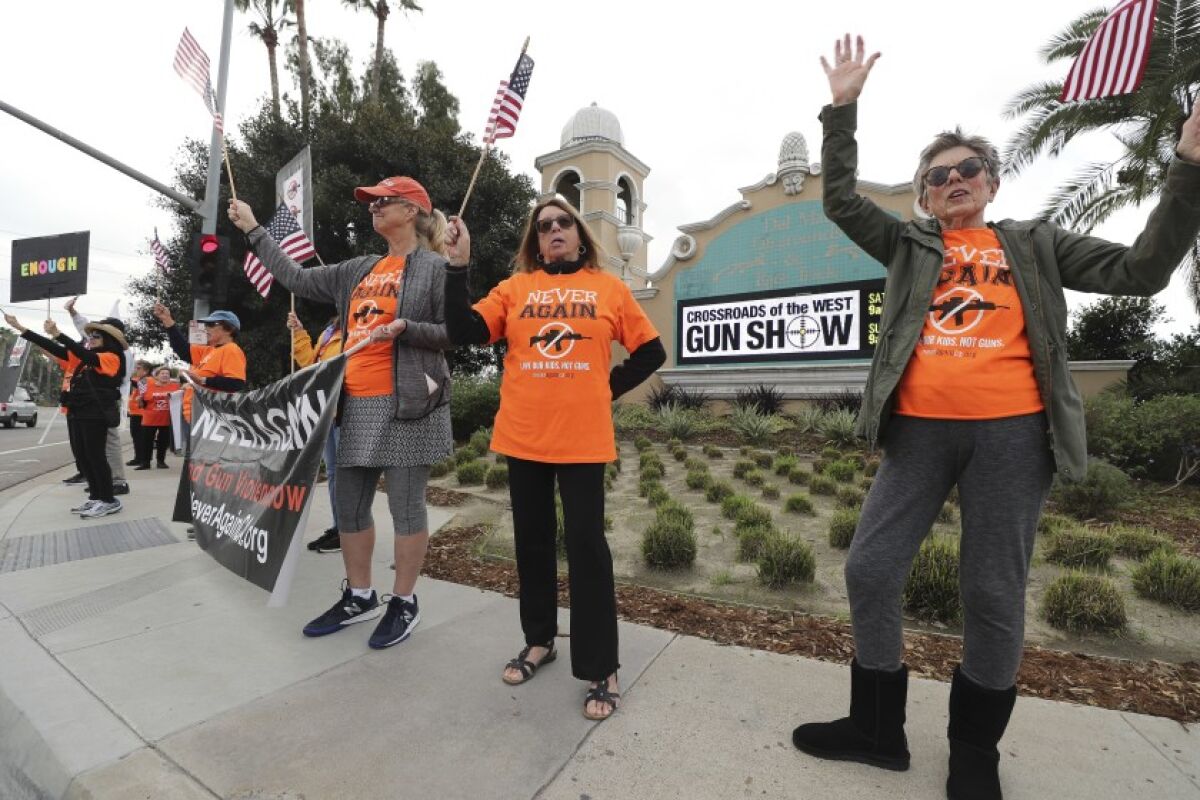 Alice McNally, right, Jane Stro, second from right, and Jill Cooper wave as motorists pass by outside the Crossroads of the West Gun Show at the Del Mar Fairgrounds in December.