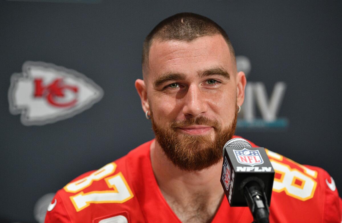 NFL star Travis Kelce speaks at a microphone while seated in his Kansas City Chiefs uniform