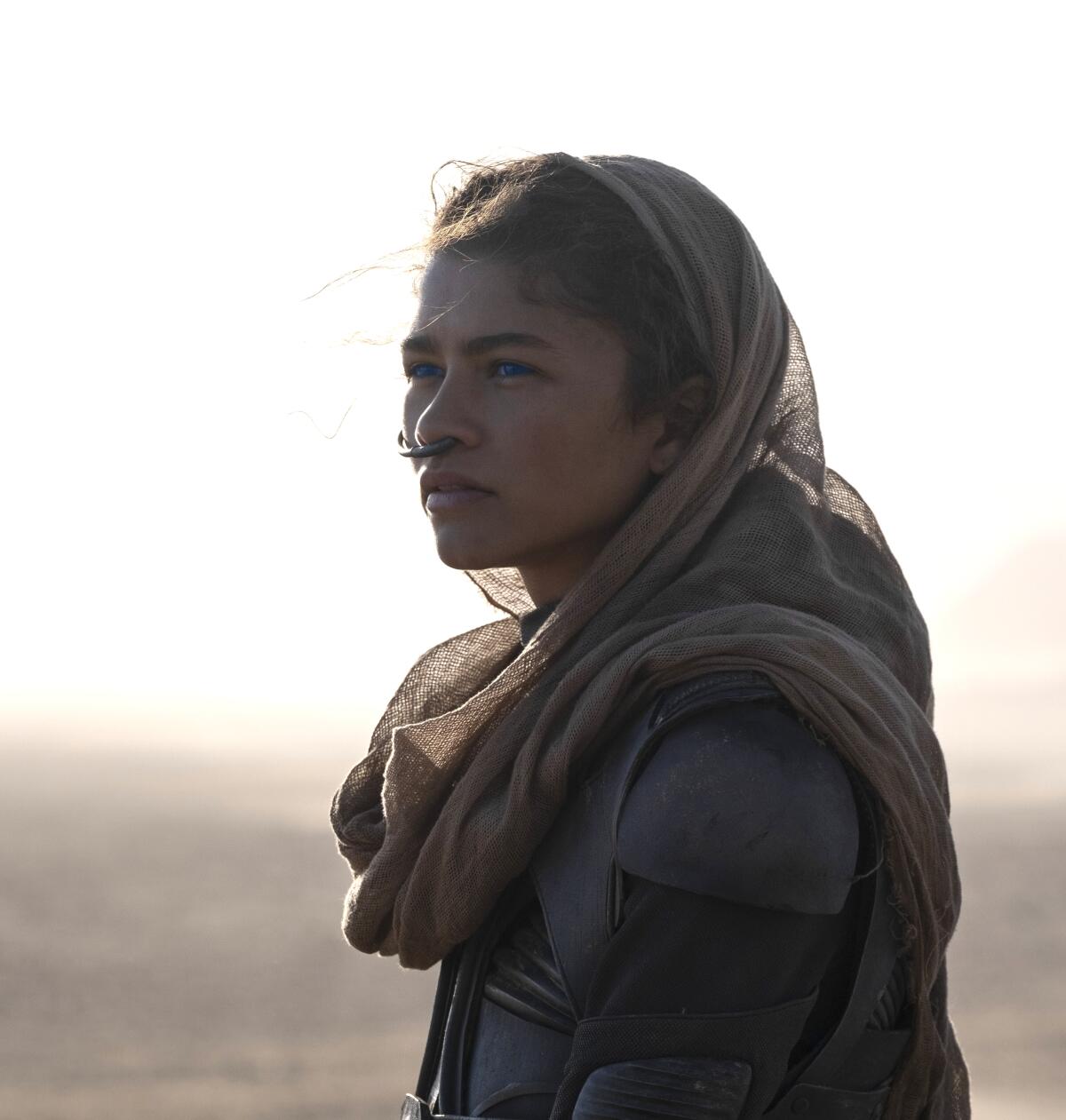 Zendaya in a desert wearing a tan headscarf, bodysuit and nose tube