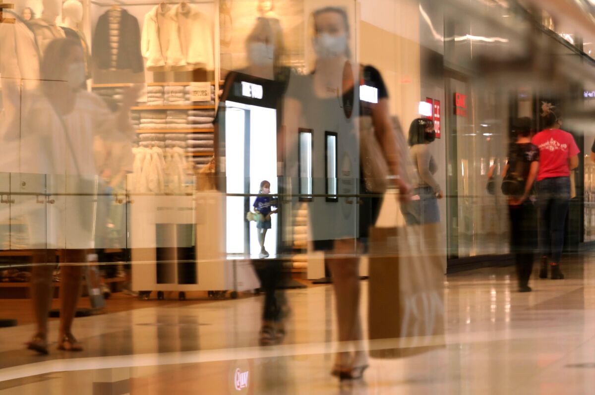 Customers, as seen through a reflection, return to indoor shopping at the Westfield Santa Anita shopping mall.