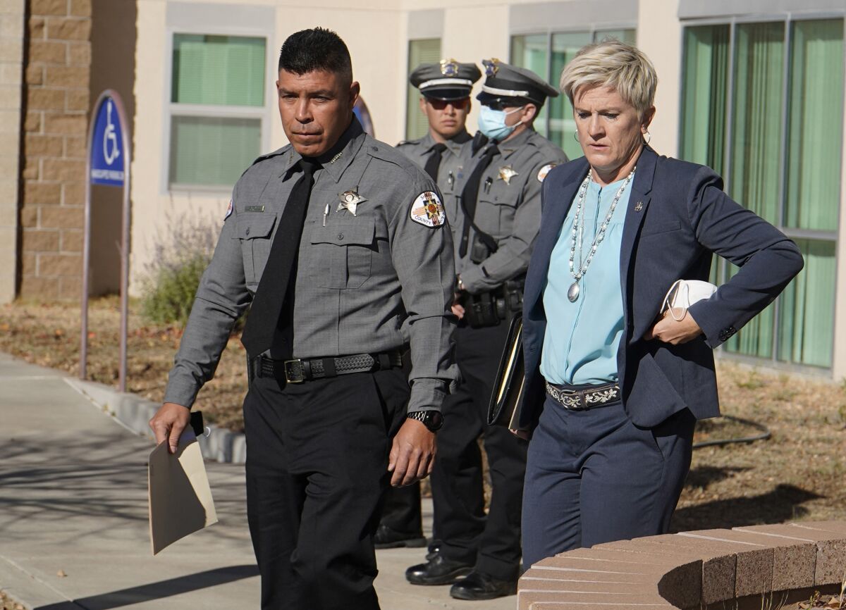 Santa Fe County Sheriff Adan Mendoza and Mary Carmack-Altwies walk together outdoors near a building.