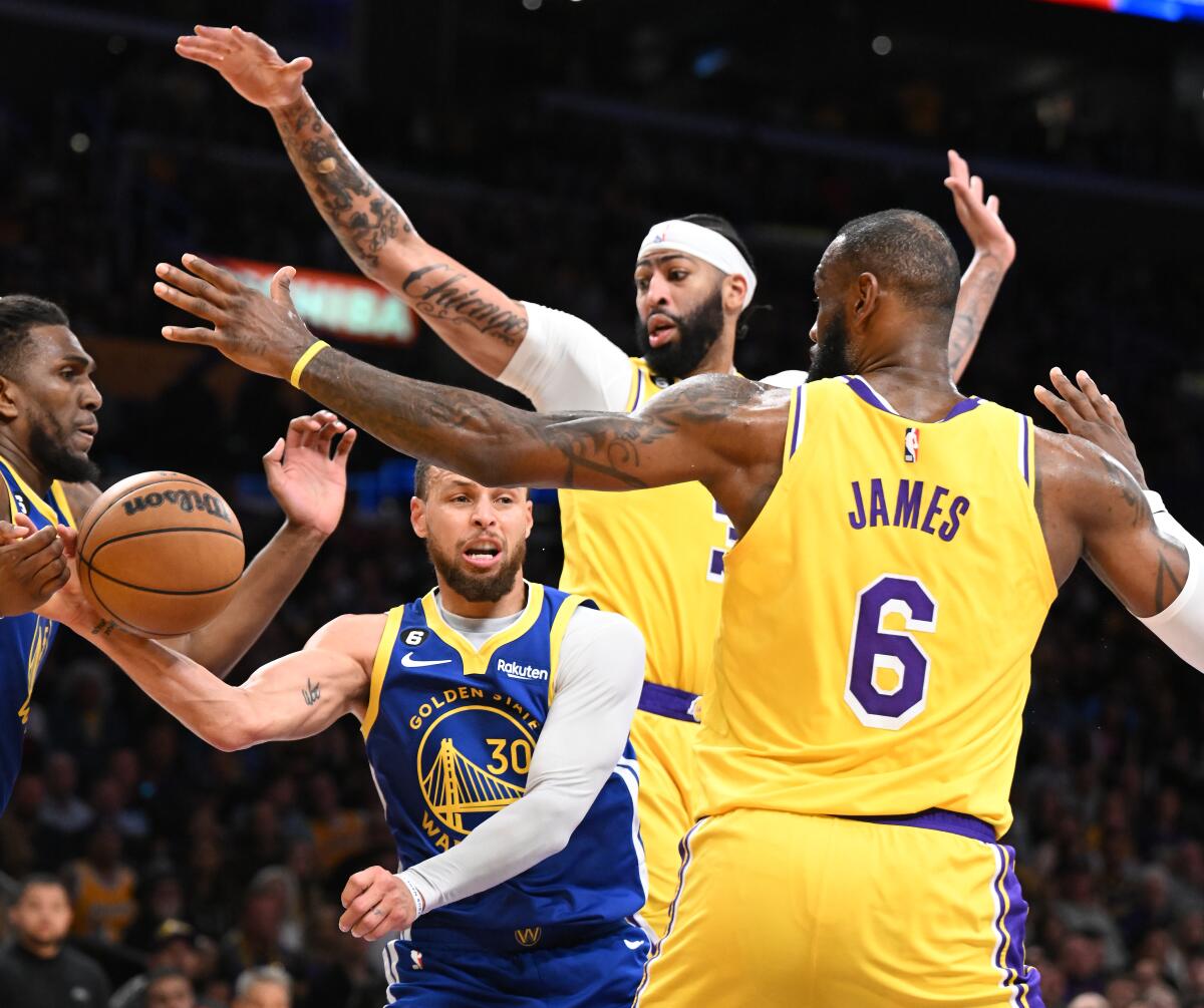 Warriors guard Stephen Curry, left, looks to pass the ball while pressured by Lakers forwards Anthony Davis and LeBron James.