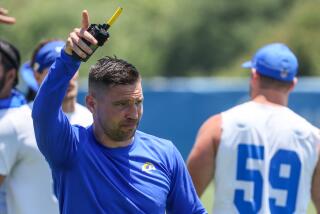 Rams defensive coordinator Chris Shula signals the team during practice with a walkie-talkie in hand.