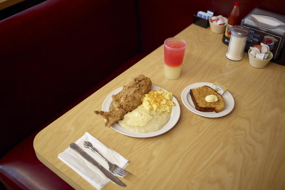 The signature dish of fried catfish, grits, eggs, a side of cornbread and a sunset soft drink on a wood-grain table.