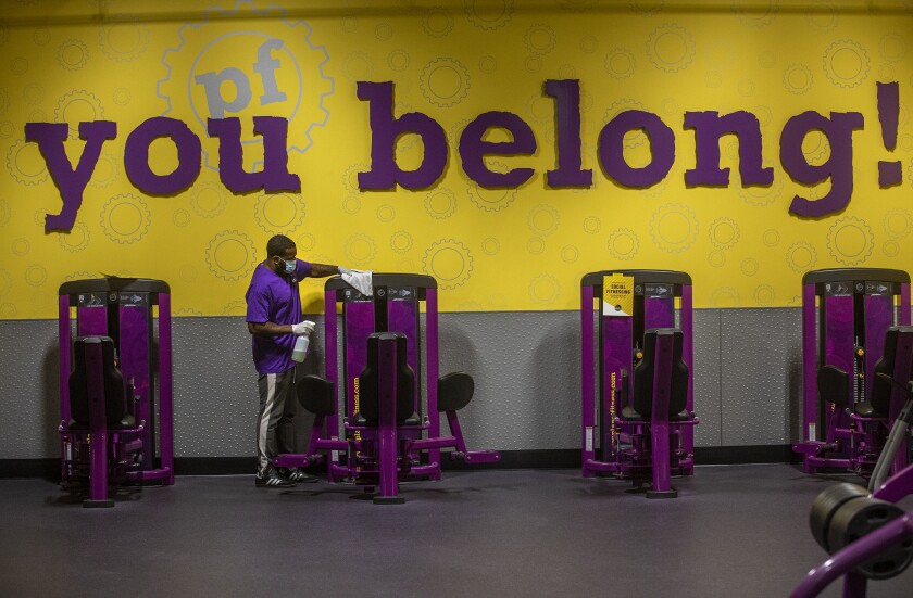 Anthony Carthan, an employee at Planet Fitness on Imperial Highway in Inglewood, disinfects exercise equipment.