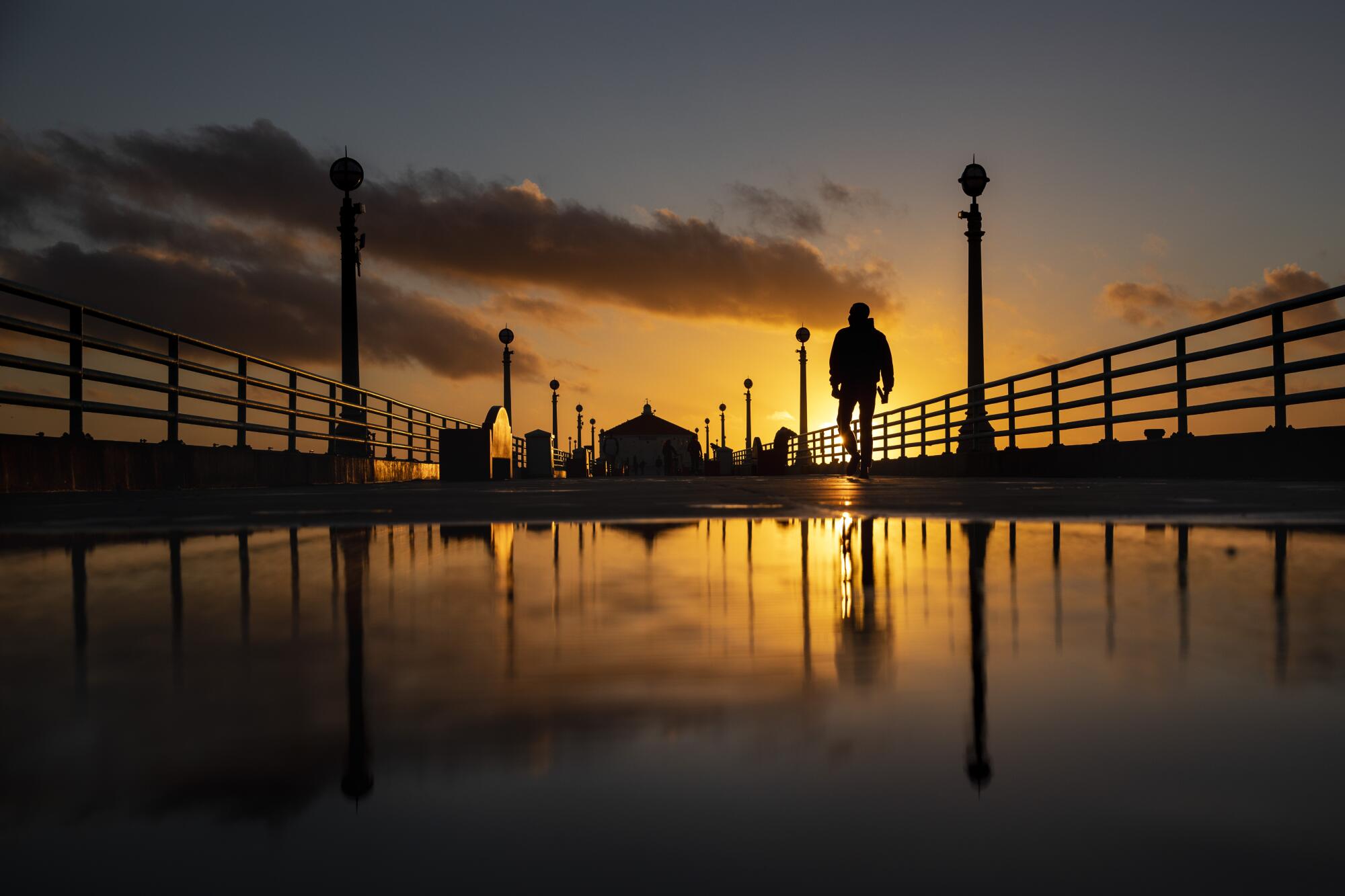 A view of a person walking on a pier at sunset 