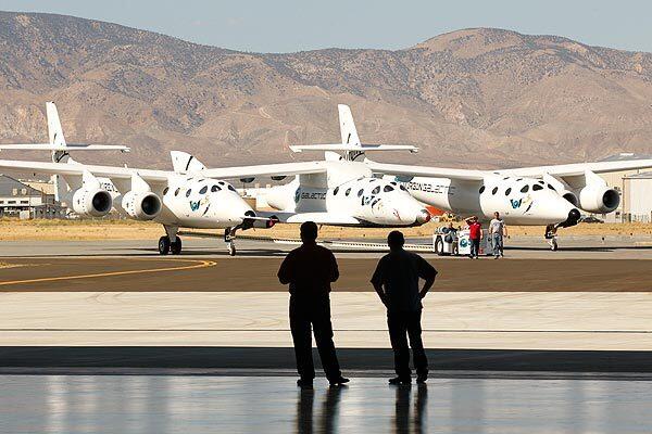 Outside the new production facility at Mojave Air and Space Port, a SpaceShipTwo rocket plane, center, is attached to the wings of a White Knight aircraft, which resembles a massive flying catamaran. See full story
