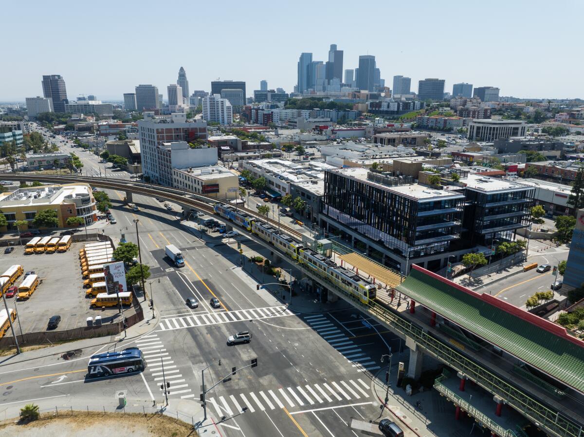 Downtown Los Angeles is visible beyond an elevated metro station and a four-story commercial building in the foreground.