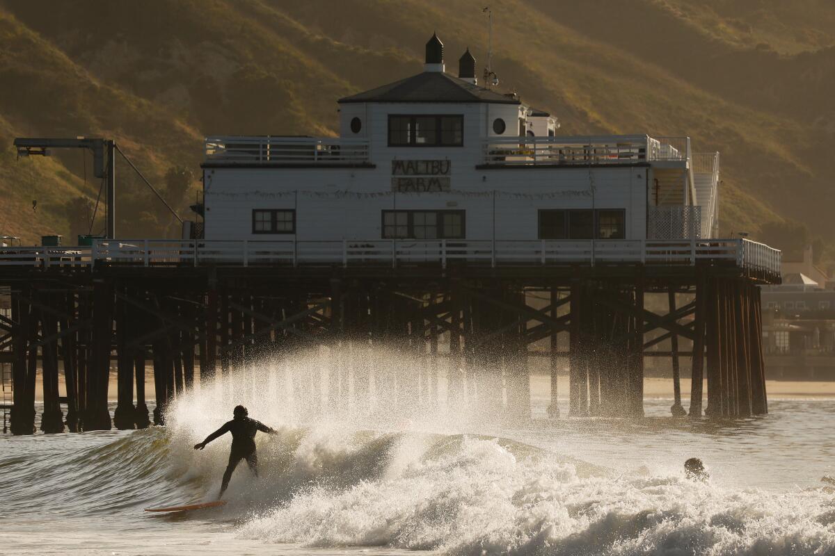 A surfer rides a wave into shore at the Malibu Pier