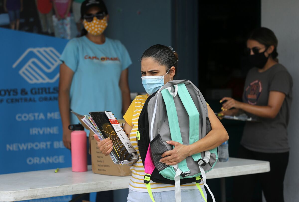 A local mom carries a new backpack for her son during a distribution of back-to-school supplies in Costa Mesa on Friday.
