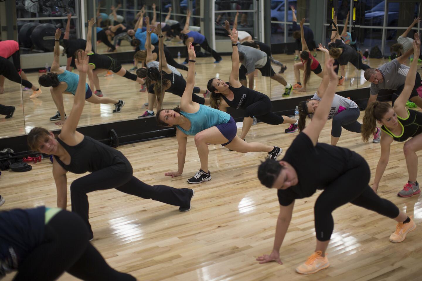 Participants stretch in unison during P90X training class at Fitness 19 in Chino.