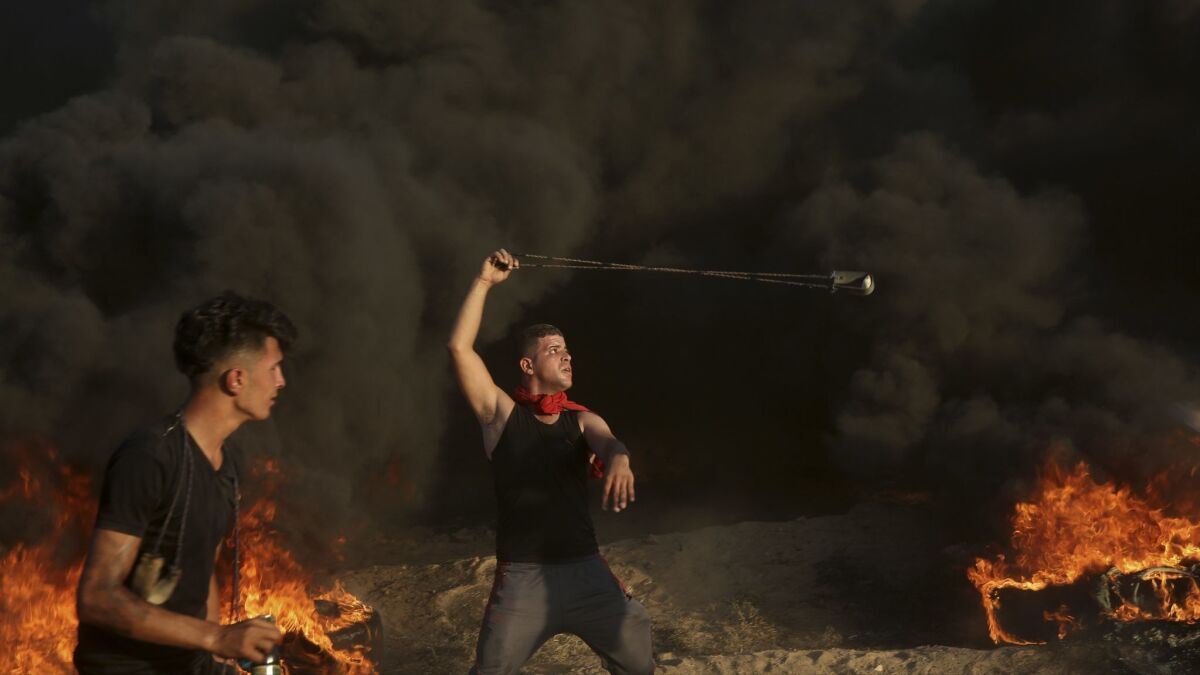 A protester hurls stones while others burn tires near the fence of the Gaza Strip border with Israel during a protest east of Gaza City on Sept. 14, 2018.